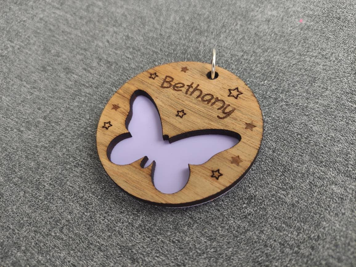 Circular keyring featuring a cut-out butterfly design backed with colourful acrylic, laser engraved with a personalised name on oak veneer.