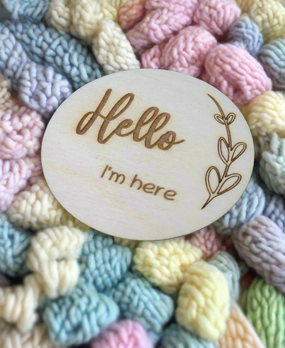 Personalised wooden milestone markers, engraved on 3mm plywood with a natural wood finish. Sized at 70mm x 70mm, they feature designs like 'Hello, I'm here' and other customisable options.