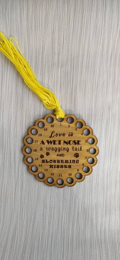 Bumpy circle-shaped thread holder with "Love is a wet nose, a wagging tail and slobbering kisses" engraved, featuring 20 holes for thread.