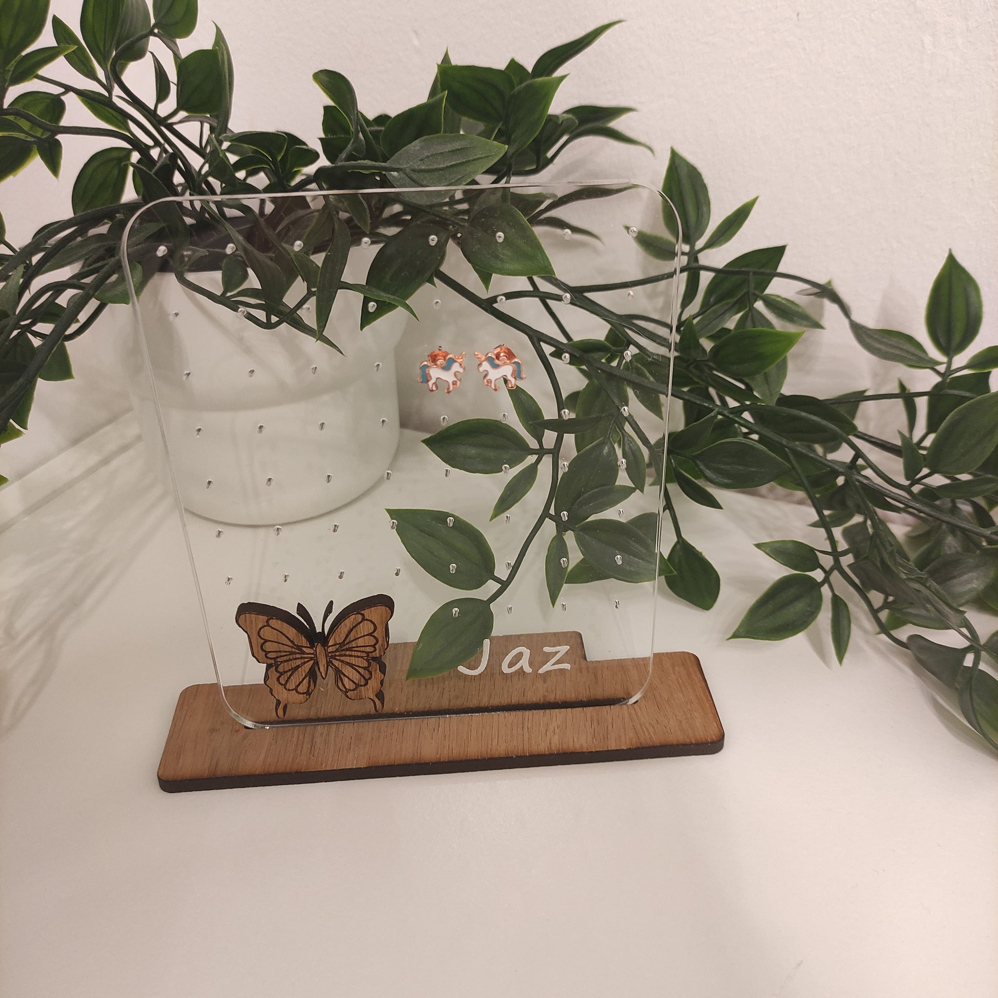Clear acrylic earring holder with a custom engraved name across the bottom and a detailed butterfly design. Holds multiple pairs of earrings, combining functionality with a cute, stylish touch. Made from 100% recycled acrylic.