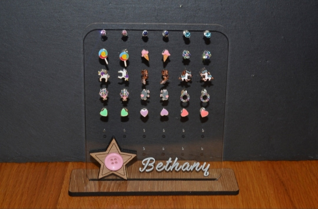 Clear acrylic earring holder with a custom engraved name across the bottom and a detailed star design. Holds multiple pairs of earrings, combining functionality with a cute, stylish touch. Made from 100% recycled acrylic.