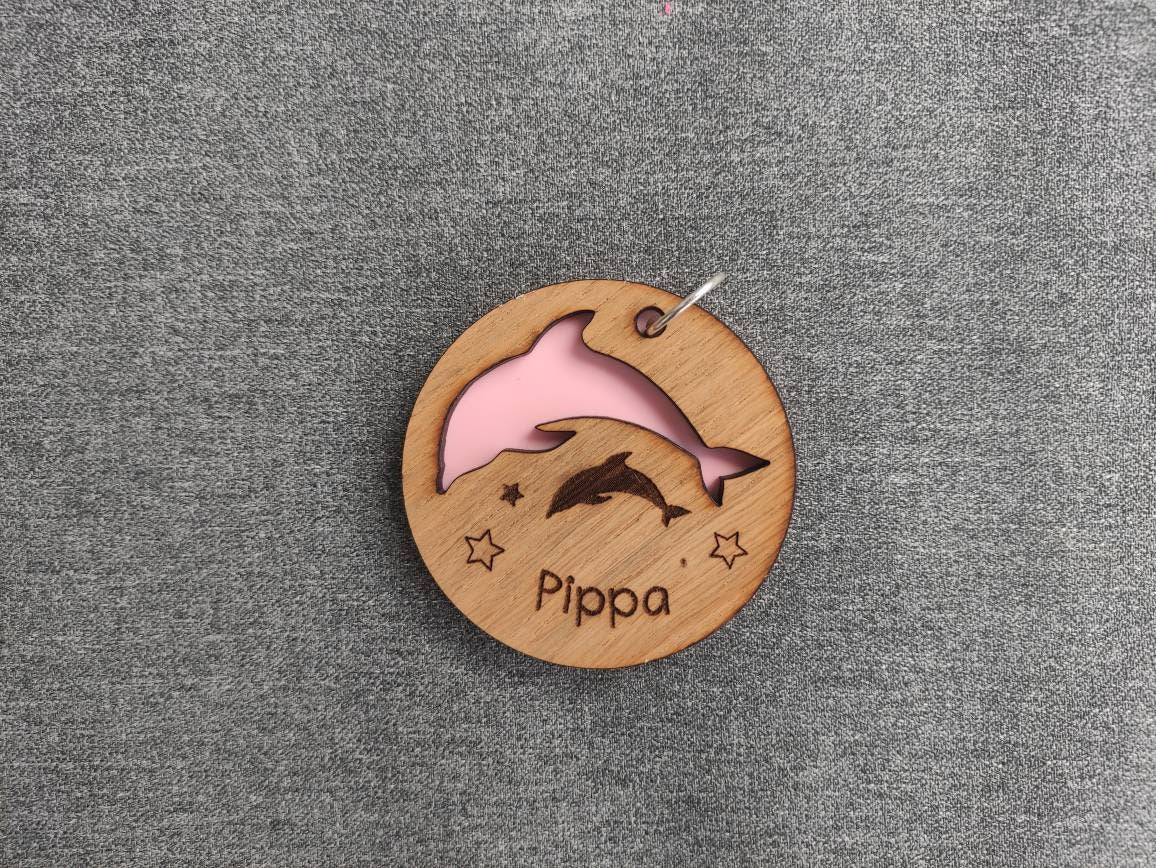 Circle keyring with a cut-out dolphin shape, backed with coloured acrylic, engraved with any name.