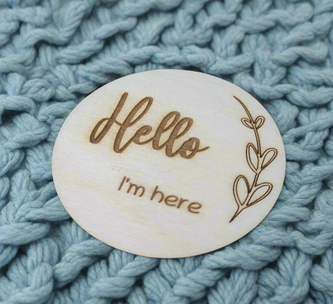 Personalised wooden milestone markers, engraved on 3mm plywood with a natural wood finish. Sized at 70mm x 70mm, they feature designs like 'Hello, I'm here' and other customisable options.