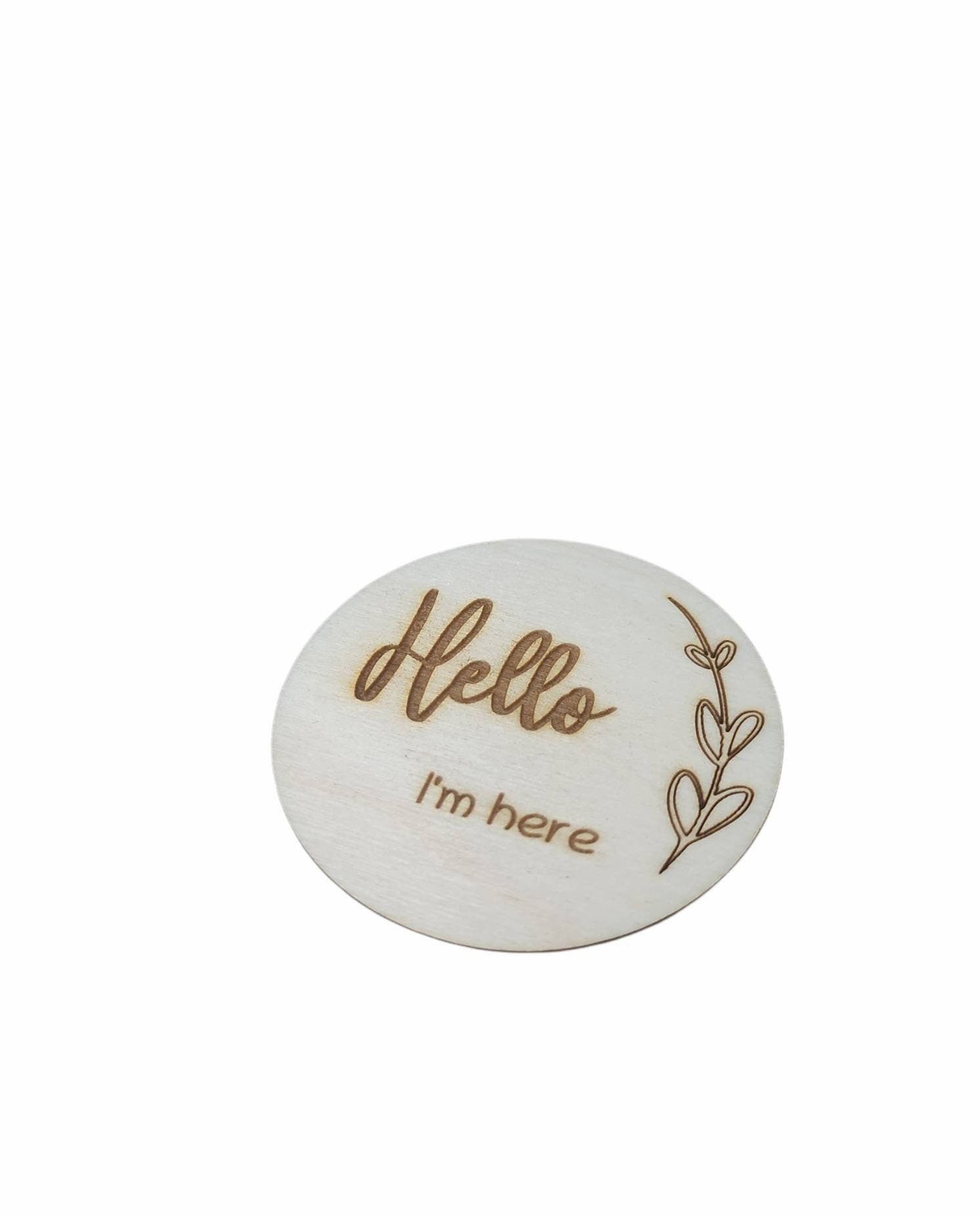 Personalised wooden milestone markers, engraved on 3mm plywood with a natural wood finish. Sized at 70mm x 70mm, they feature designs like 'Hello, I'm here' and other customisable options.