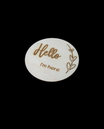 Personalised wooden milestone markers, engraved on 3mm plywood with a natural wood finish. Sized at 70mm x 70mm, they feature designs like 'Hello, I'm here' and other customisable options.