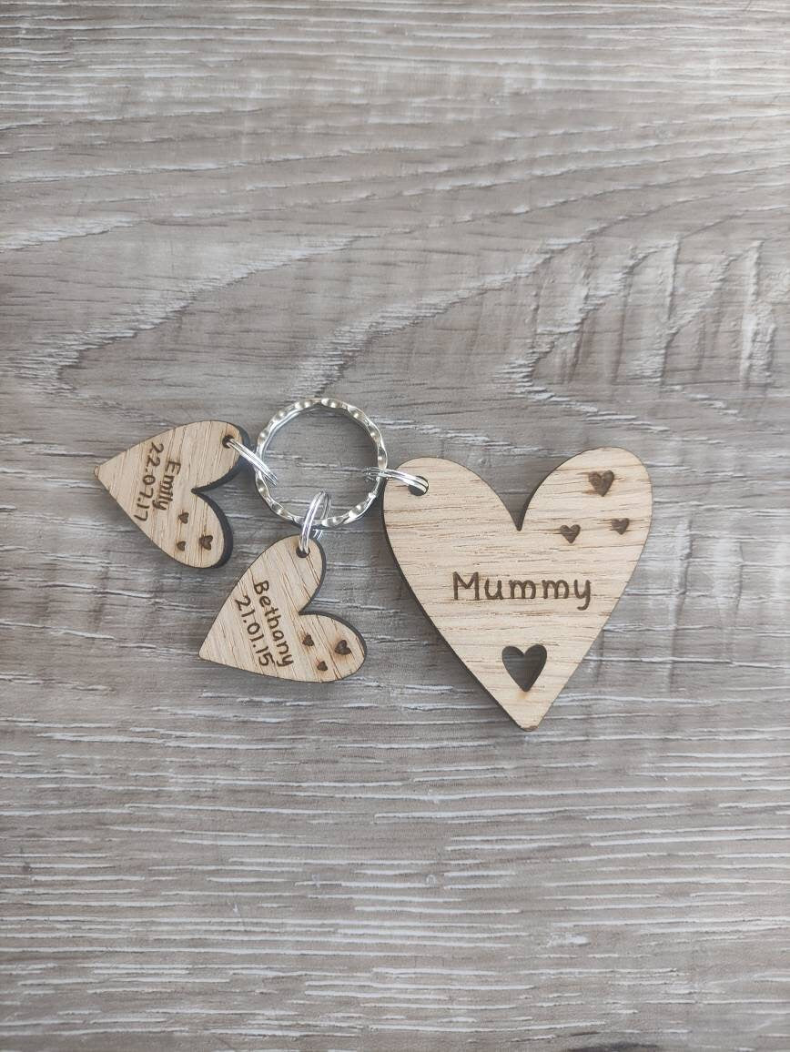 Personalised heart-shaped wooden keyring engraved with "Mummy" and customisable with charms featuring a child’s name and date of birth.
