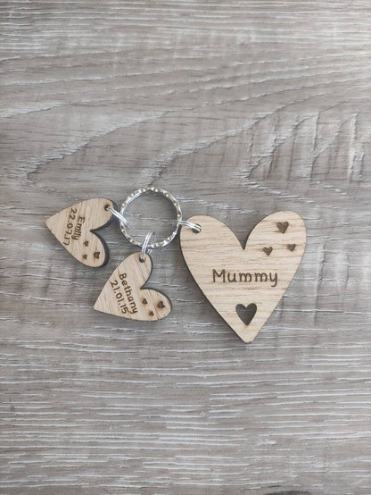 Personalised heart-shaped wooden keyring engraved with "Mummy" and customisable with charms featuring a child’s name and date of birth.