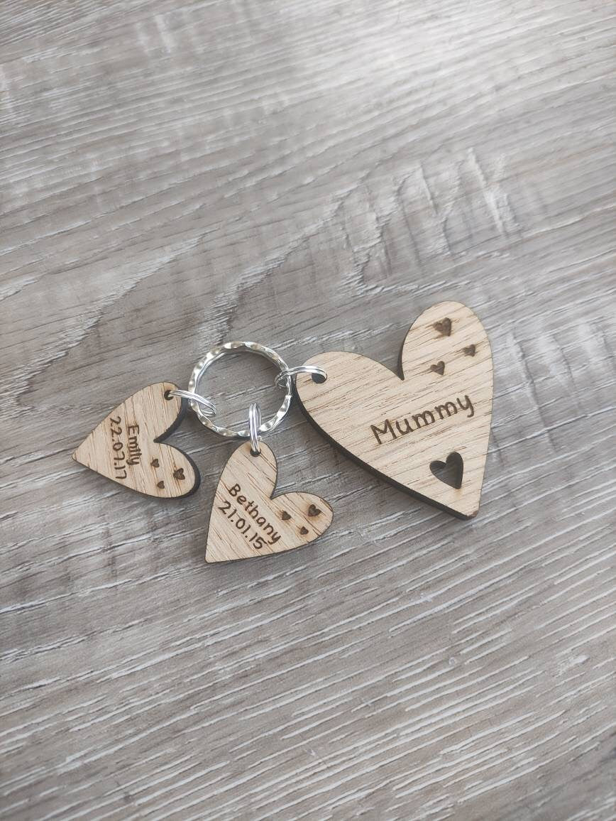 Personalised heart-shaped wooden keyring engraved with "Mummy" and customisable with charms featuring a child’s name and date of birth.