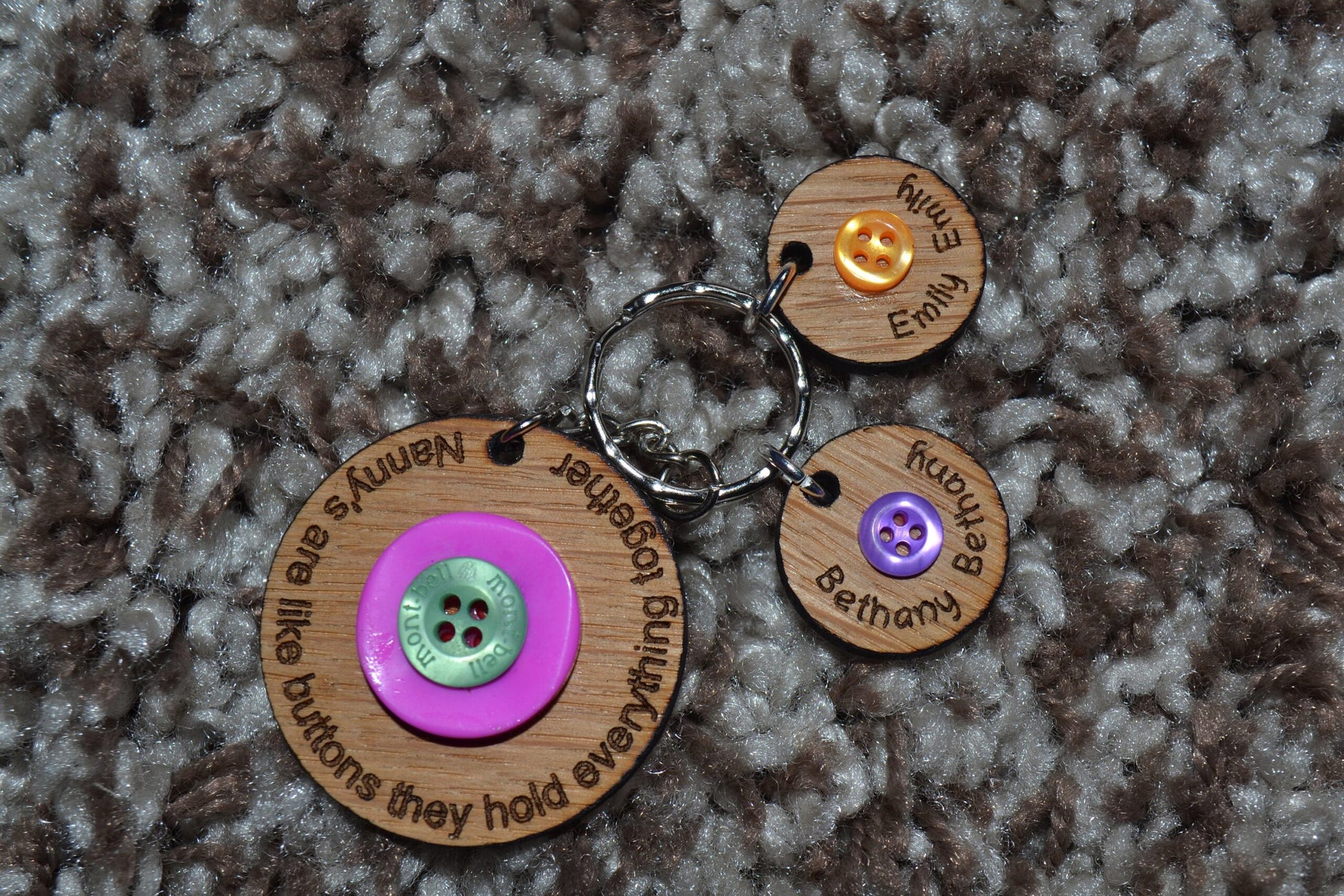 Circle keyring engraved with 'Mum's are like buttons, they hold everything together' around the edge. Two buttons in the middle, with personalised charms featuring children's names and coloured buttons.