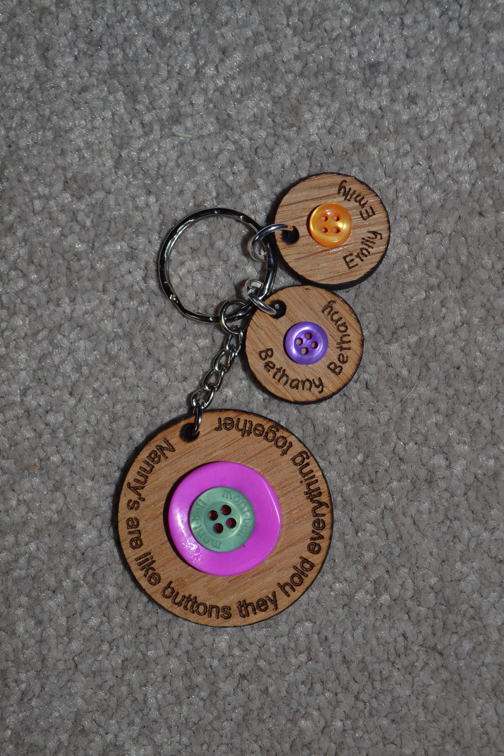 Circle keyring engraved with 'Mum's are like buttons, they hold everything together' around the edge. Two buttons in the middle, with personalised charms featuring children's names and coloured buttons.