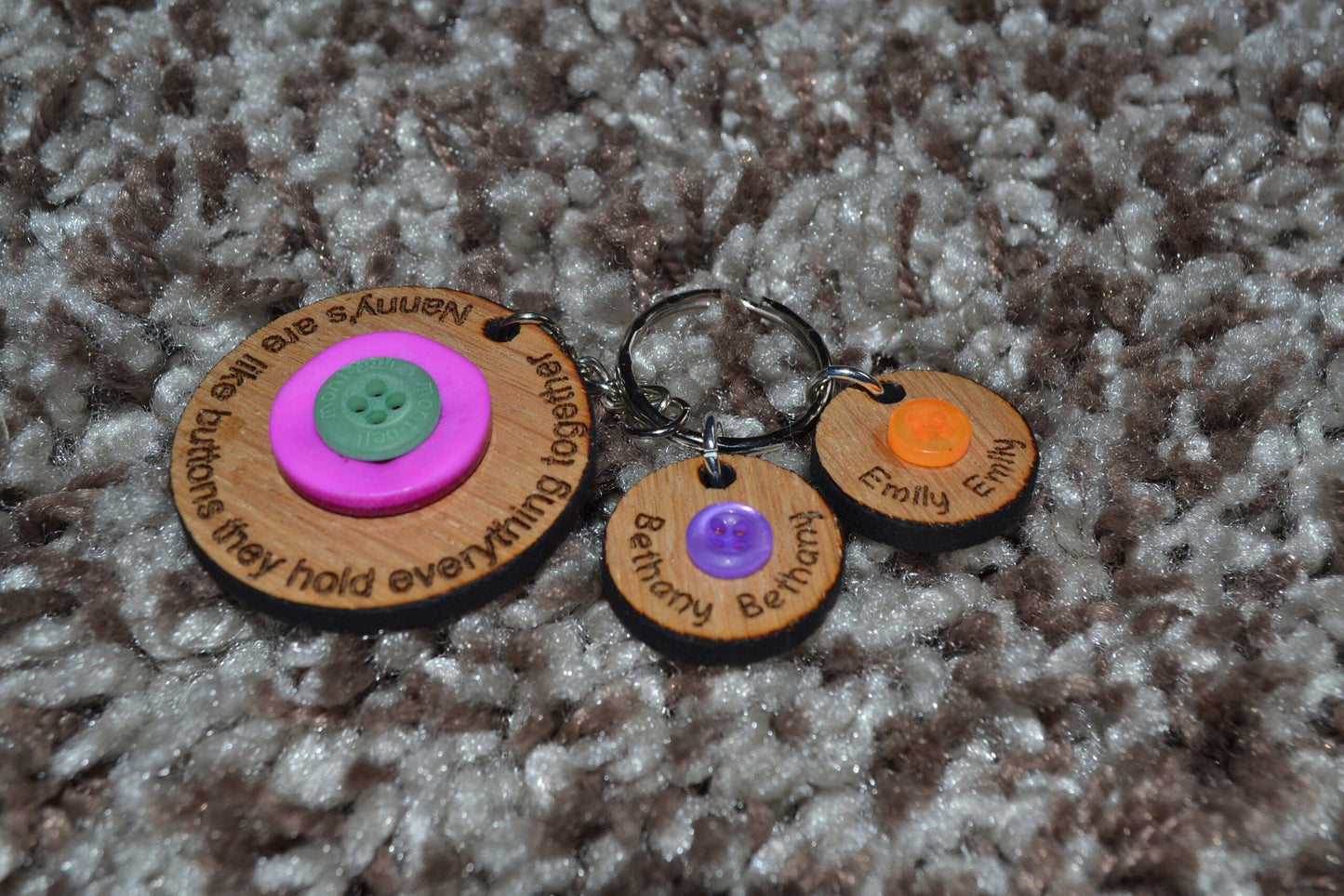 Circle keyring engraved with 'Mum's are like buttons, they hold everything together' around the edge. Two buttons in the middle, with personalised charms featuring children's names and coloured buttons.