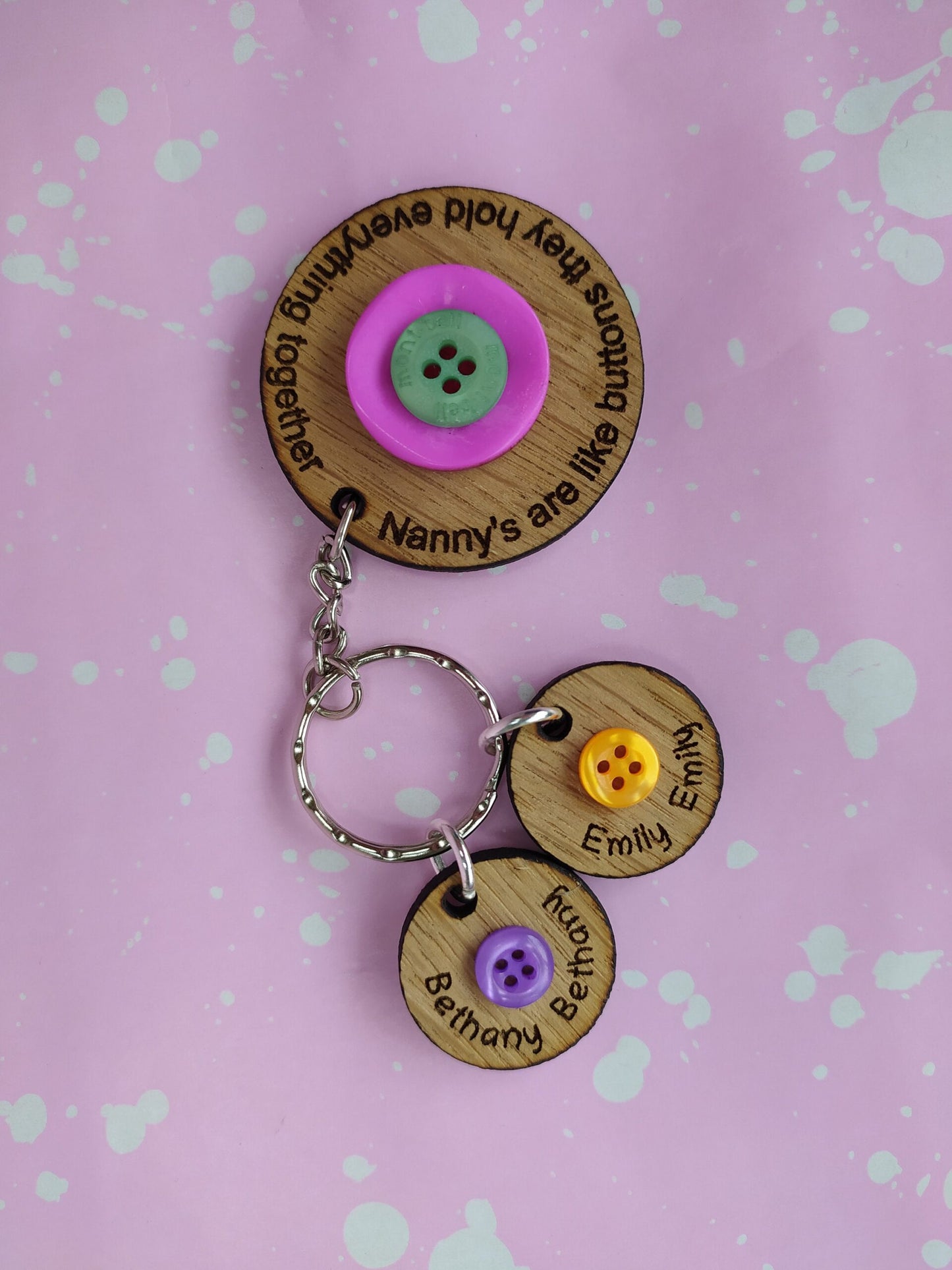 Circle keyring engraved with 'Mum's are like buttons, they hold everything together' around the edge. Two buttons in the middle, with personalised charms featuring children's names and coloured buttons.