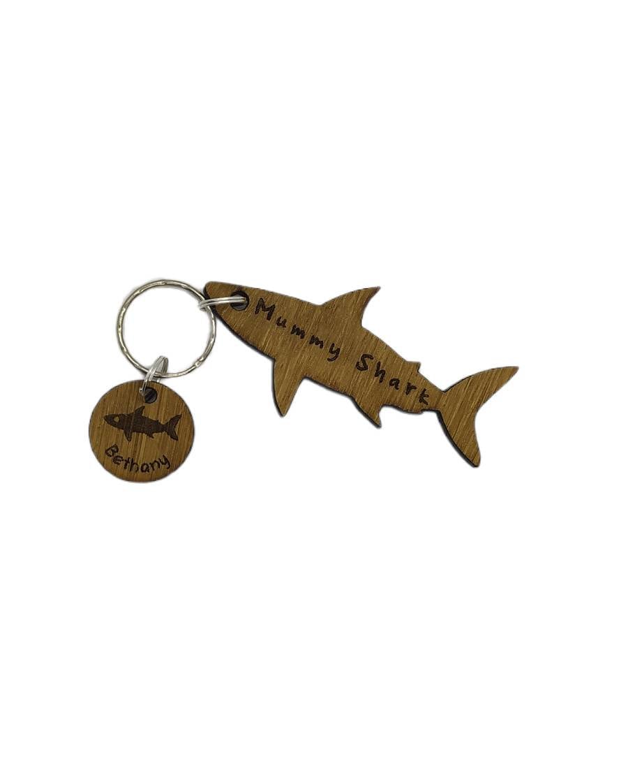 Shark-shaped keyring with "Mummy Shark" engraved, featuring child name charms around the outside and a shark in the middle.