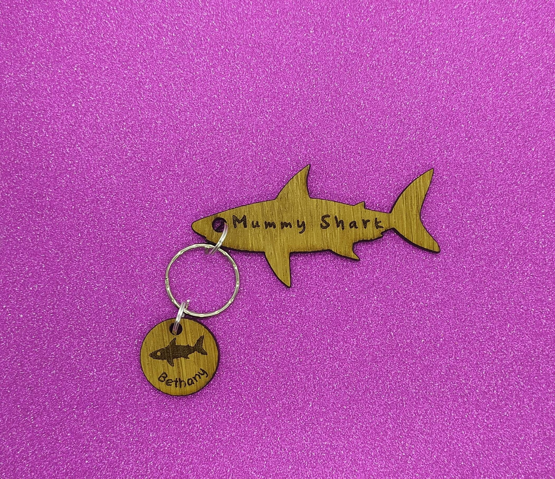 Shark-shaped keyring with "Mummy Shark" engraved, featuring child name charms around the outside and a shark in the middle.