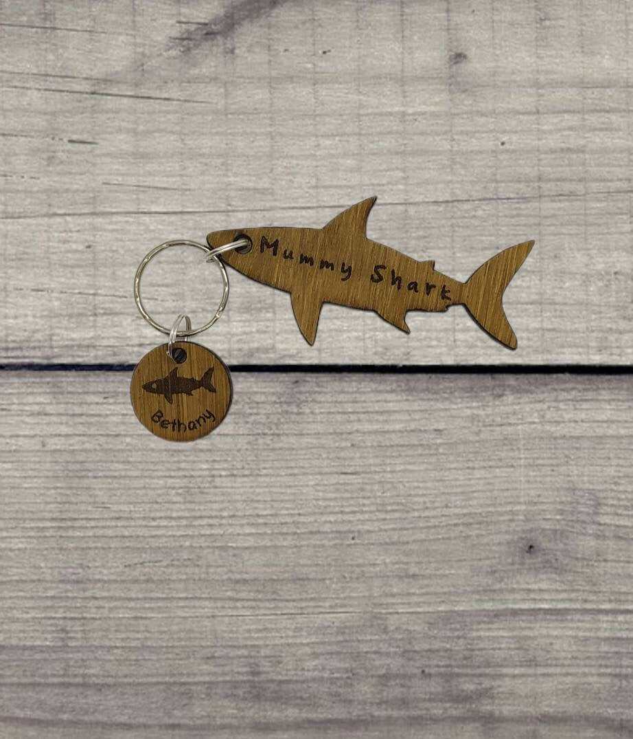 Shark-shaped keyring with "Mummy Shark" engraved, featuring child name charms around the outside and a shark in the middle.