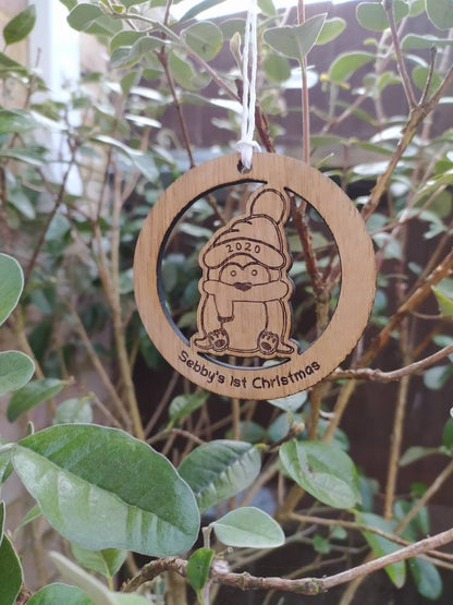Personalised circular wooden bauble featuring a laser-engraved penguin in the centre, with the year engraved on its hat and "First Christmas" along with a custom name engraved around the edge. Perfect keepsake ornament for the Christmas tree.