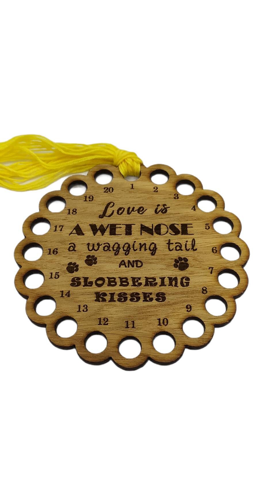 Bumpy circle-shaped thread holder with "Love is a wet nose, a wagging tail and slobbering kisses" engraved, featuring 20 holes for thread.