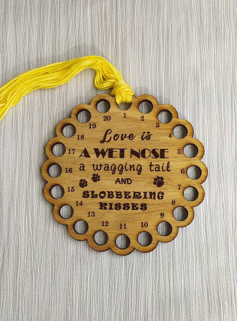 Bumpy circle-shaped thread holder with "Love is a wet nose, a wagging tail and slobbering kisses" engraved, featuring 20 holes for thread.