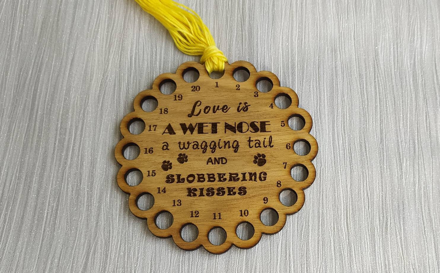 Bumpy circle-shaped thread holder with "Love is a wet nose, a wagging tail and slobbering kisses" engraved, featuring 20 holes for thread.