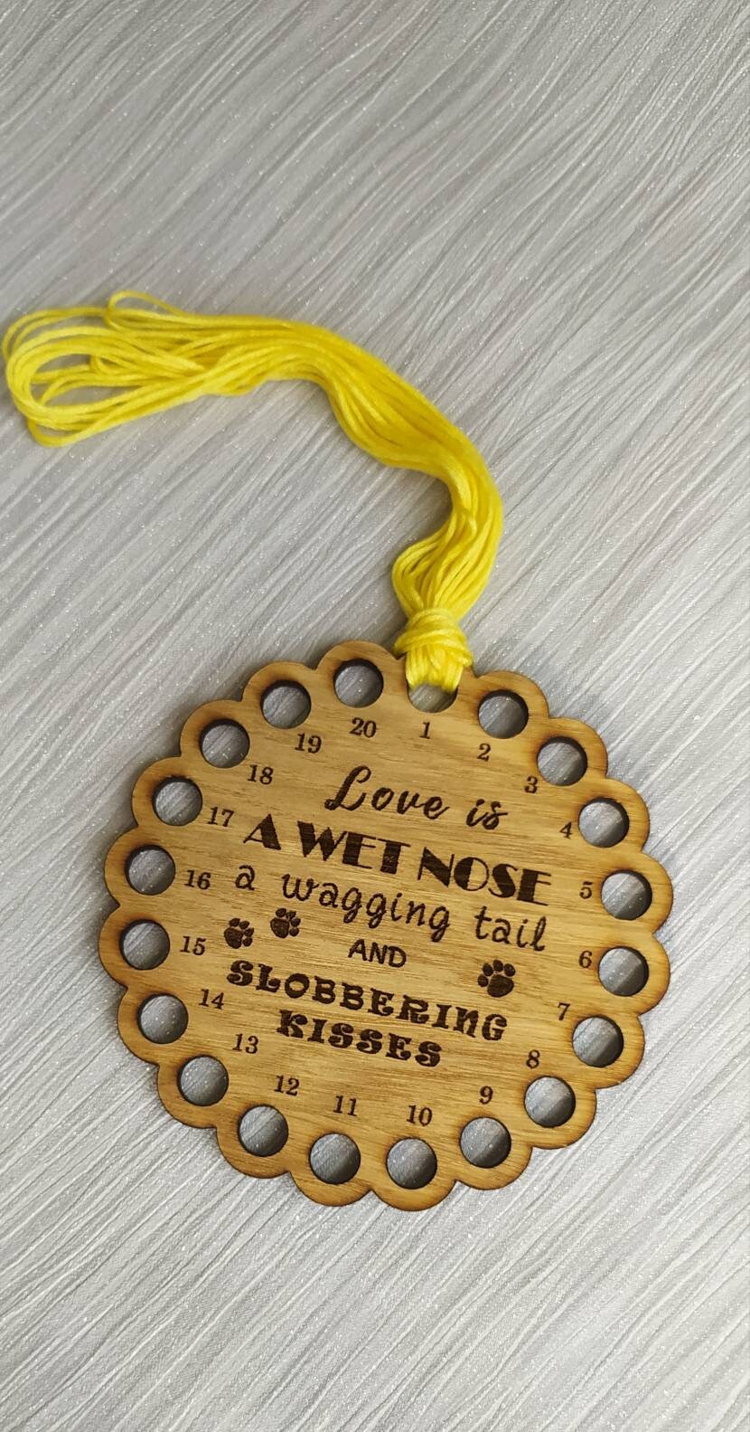 Bumpy circle-shaped thread holder with "Love is a wet nose, a wagging tail and slobbering kisses" engraved, featuring 20 holes for thread.