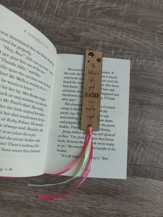 Wooden bookmark engraved with the quote "The influence of a good TEACHER can never be erased," featuring floral designs and a coloured ribbon at the bottom.