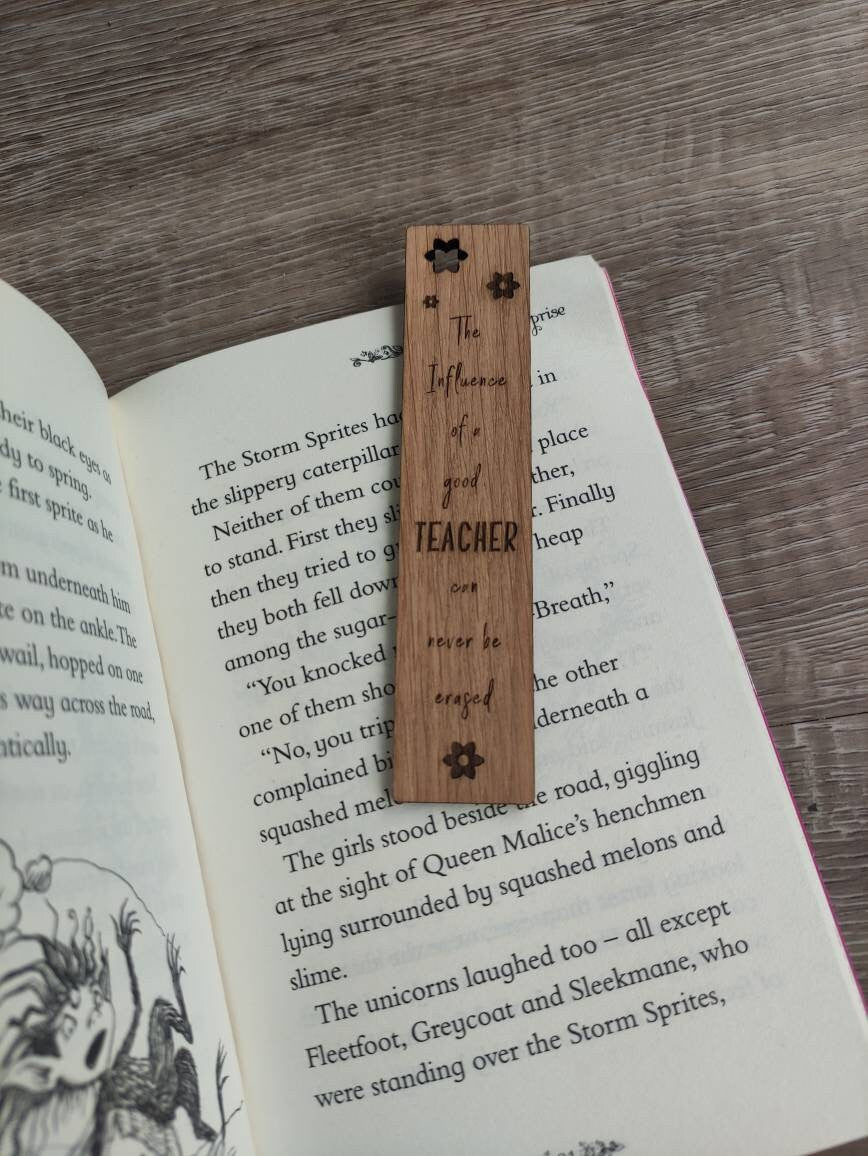 Wooden bookmark engraved with the quote "The influence of a good TEACHER can never be erased," featuring floral designs and a coloured ribbon at the bottom.