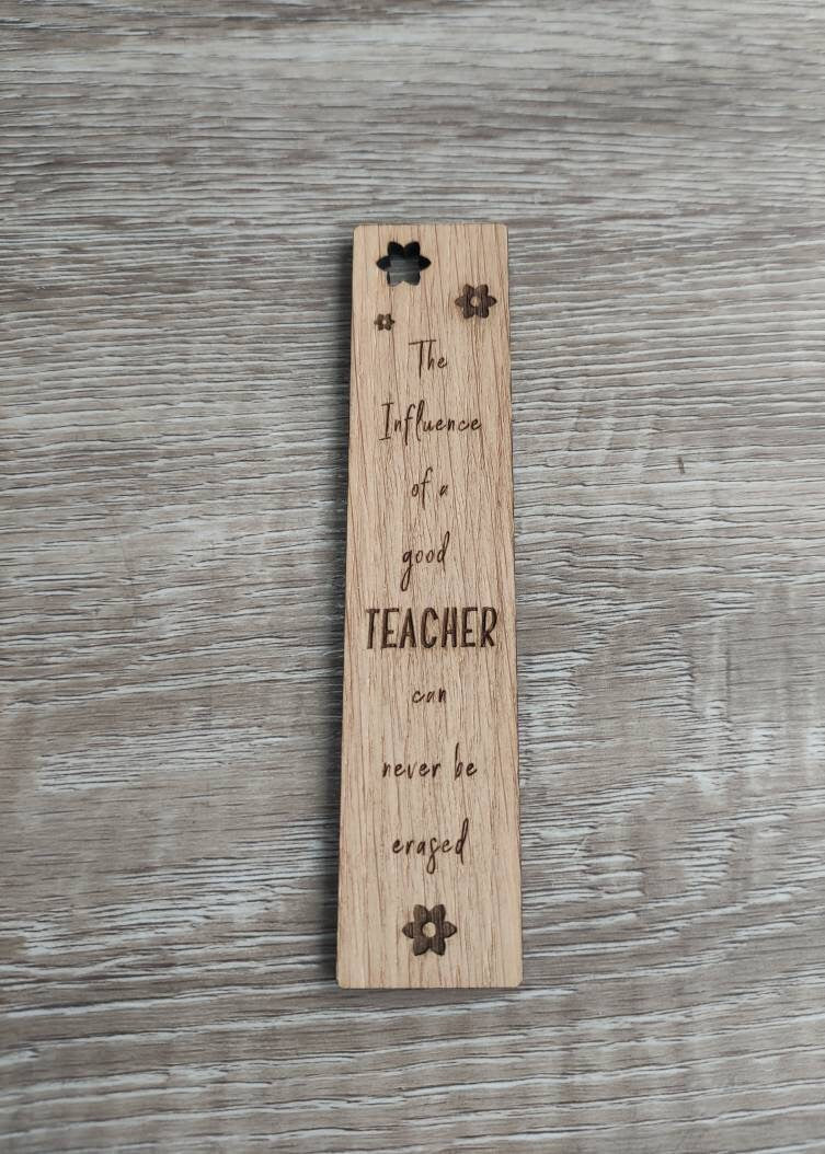 Wooden bookmark engraved with the quote "The influence of a good TEACHER can never be erased," featuring floral designs and a coloured ribbon at the bottom.