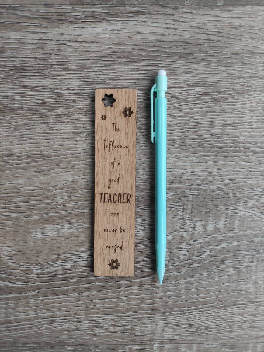 Wooden bookmark engraved with the quote "The influence of a good TEACHER can never be erased," featuring floral designs and a coloured ribbon at the bottom.