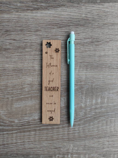 Wooden bookmark engraved with the quote "The influence of a good TEACHER can never be erased," featuring floral designs and a coloured ribbon at the bottom.