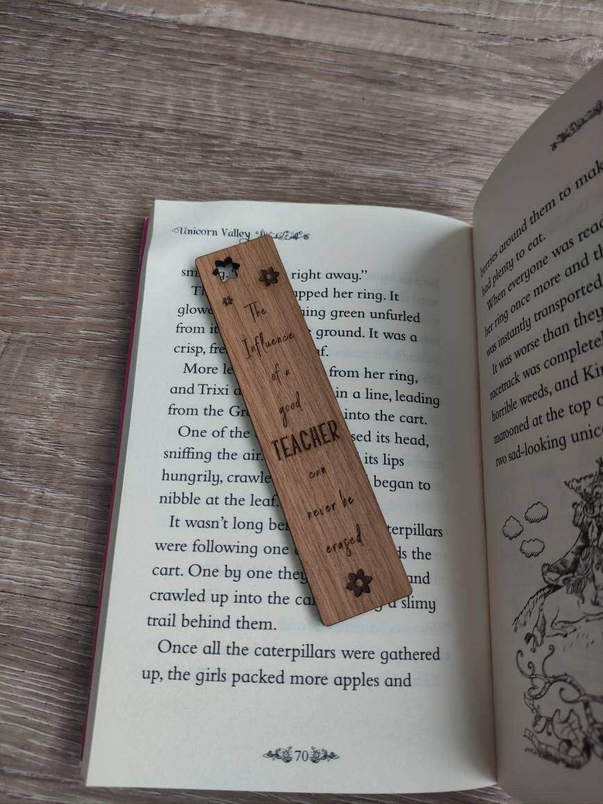 Wooden bookmark engraved with the quote "The influence of a good TEACHER can never be erased," featuring floral designs and a coloured ribbon at the bottom.