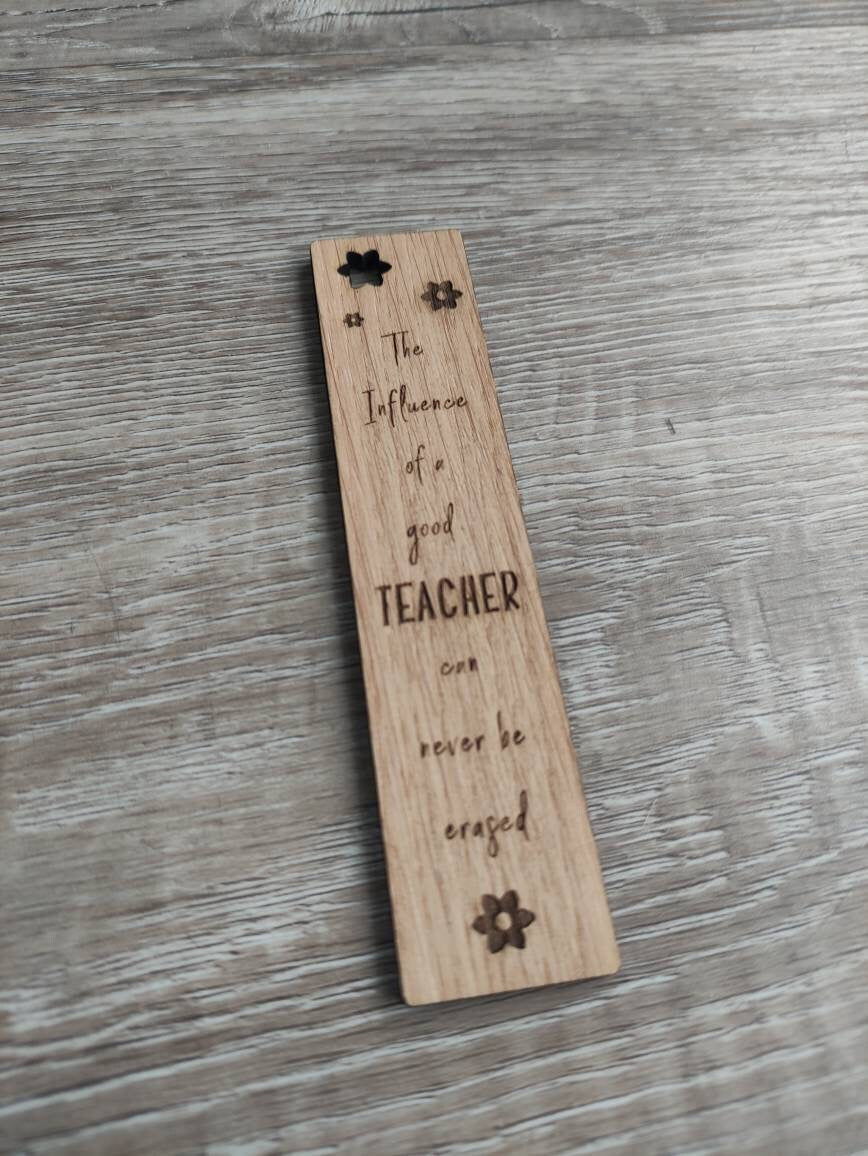 Wooden bookmark engraved with the quote "The influence of a good TEACHER can never be erased," featuring floral designs and a coloured ribbon at the bottom.