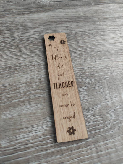 Wooden bookmark engraved with the quote "The influence of a good TEACHER can never be erased," featuring floral designs and a coloured ribbon at the bottom.