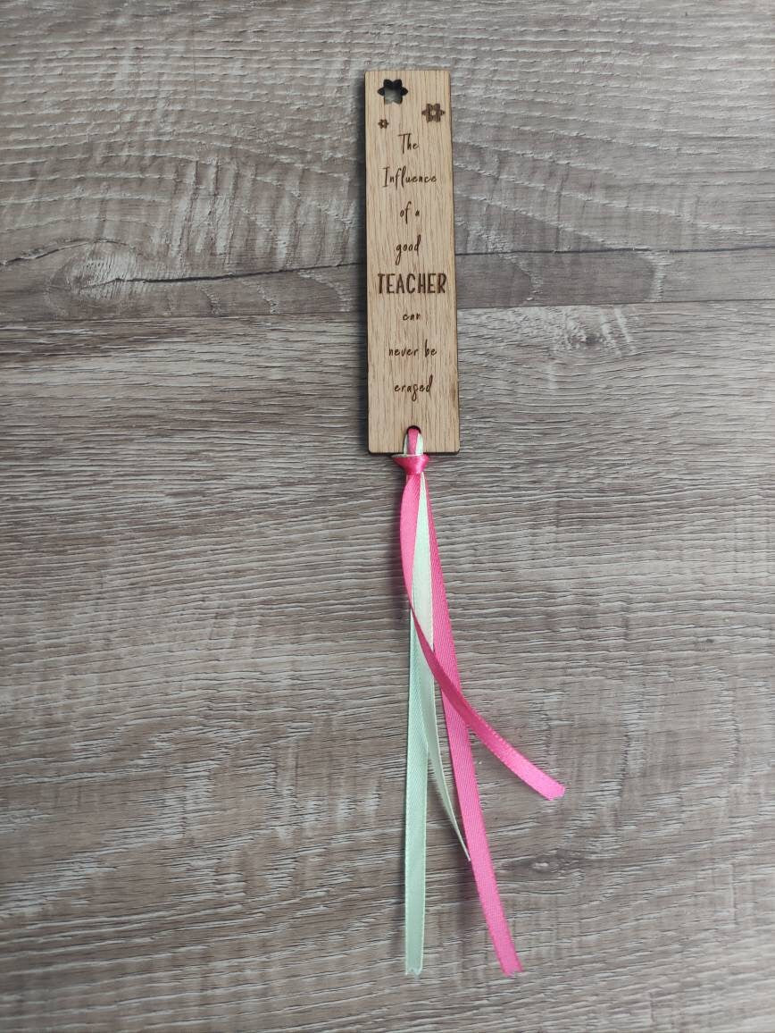 Wooden bookmark engraved with the quote "The influence of a good TEACHER can never be erased," featuring floral designs and a coloured ribbon at the bottom.
