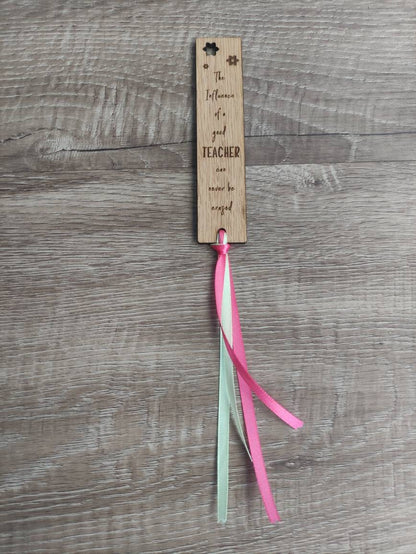 Wooden bookmark engraved with the quote "The influence of a good TEACHER can never be erased," featuring floral designs and a coloured ribbon at the bottom.