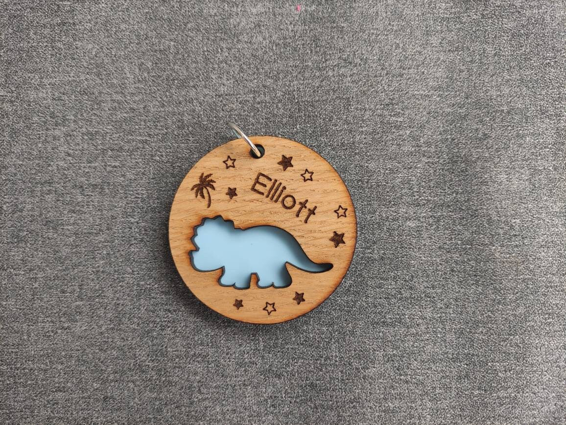 Round wooden keyring with a cut-out triceratops design, personalised with an engraved name, backed with colourful acrylic.