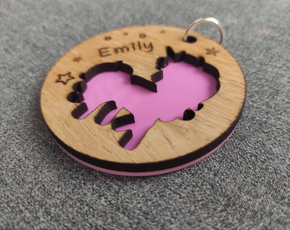 Circular wooden keyring with a unicorn cut-out, backed with colourful acrylic and personalised with an engraved name.